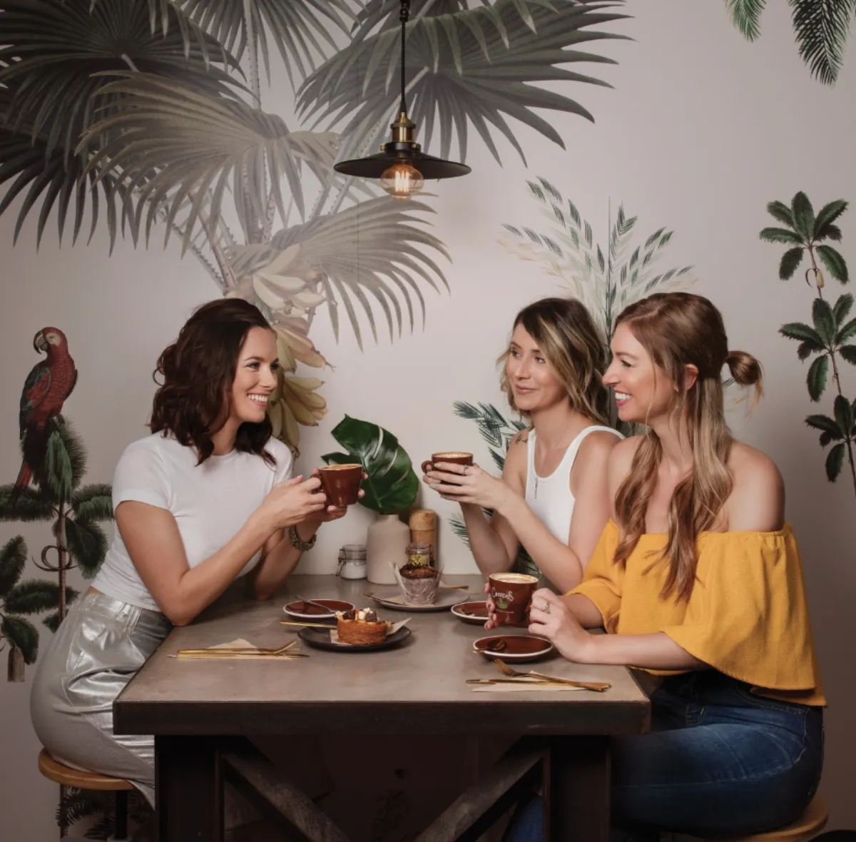 Inside Sweet Brew & Co — tropical wallpaper, warm ambiance and guests enjoying coffee